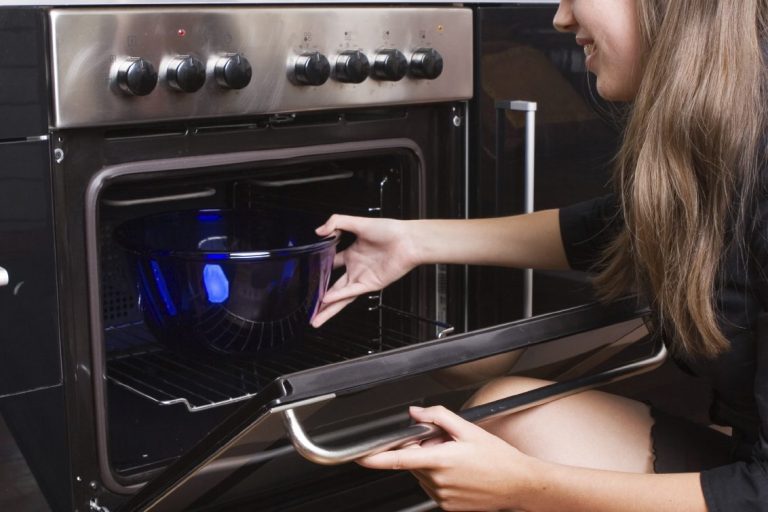 Persona sacando un recipiente del horno, con luz interior encendida.