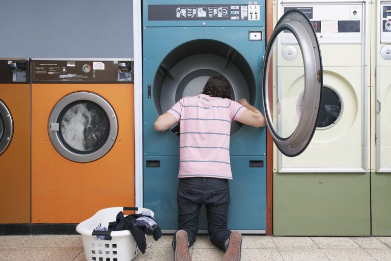 Persona agachada mirando dentro de una lavadora en una lavandería.